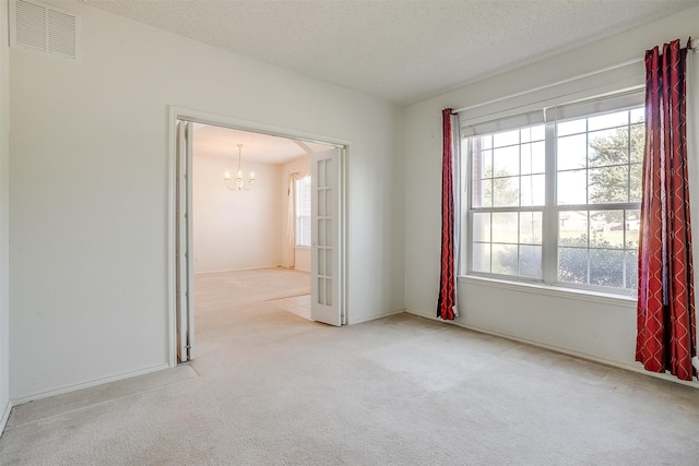 carpeted empty room with a notable chandelier and a textured ceiling