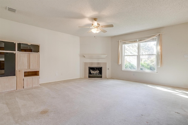 unfurnished living room featuring ceiling fan, light colored carpet, a textured ceiling, and a tile fireplace