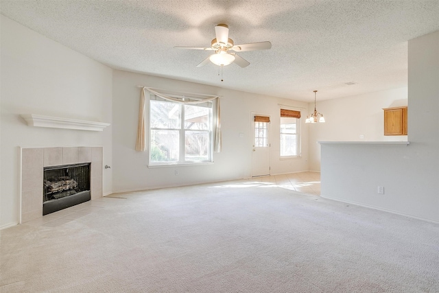 unfurnished living room with ceiling fan with notable chandelier, a tiled fireplace, and light colored carpet