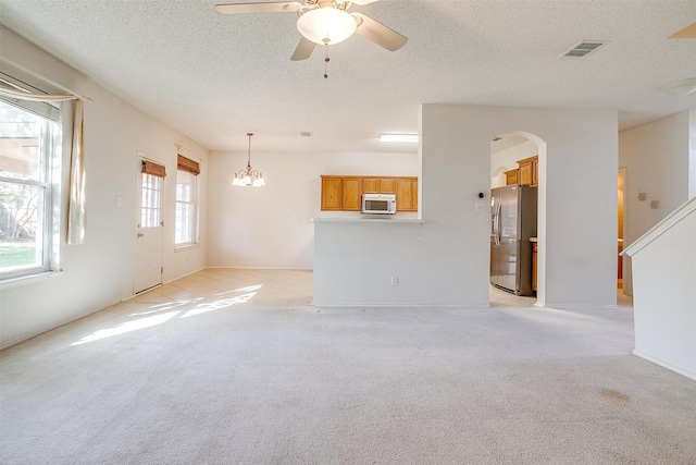 unfurnished living room featuring light colored carpet, a textured ceiling, and ceiling fan with notable chandelier