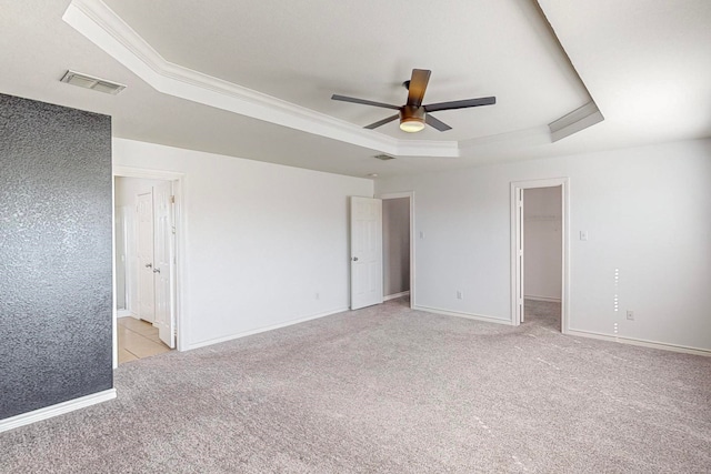 unfurnished bedroom with a raised ceiling, a closet, ceiling fan, a walk in closet, and ornamental molding