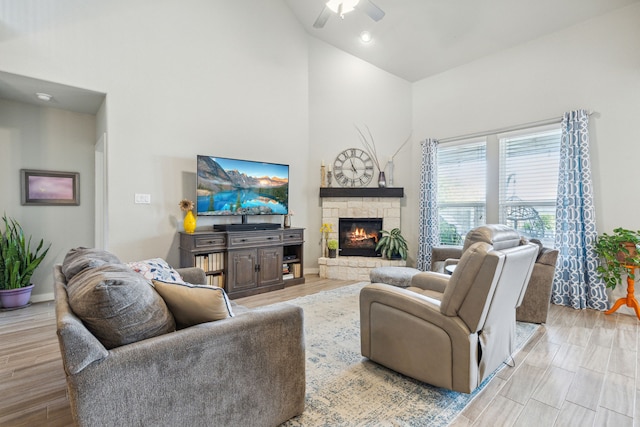 living room with ceiling fan with notable chandelier, a high ceiling, hardwood / wood-style floors, and a stone fireplace