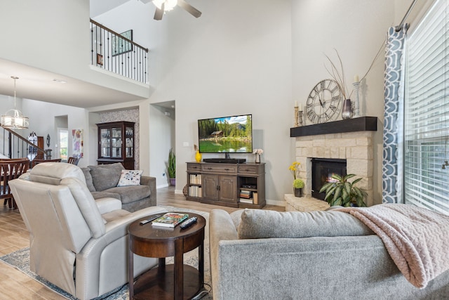 living room featuring a stone fireplace, light wood-type flooring, sink, high vaulted ceiling, and ceiling fan