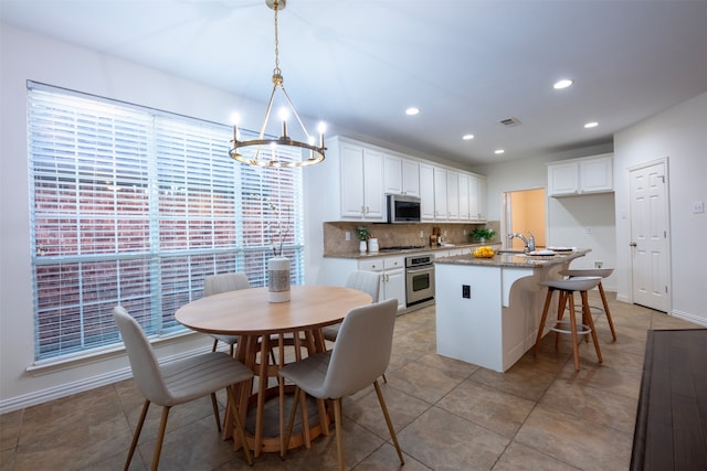 kitchen featuring appliances with stainless steel finishes, a kitchen island with sink, pendant lighting, and white cabinetry