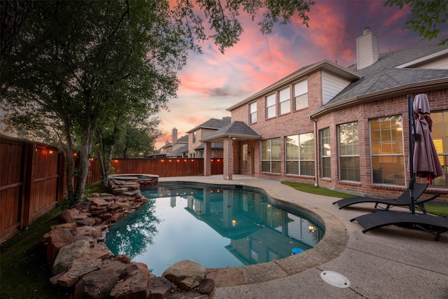 pool at dusk with an in ground hot tub and a patio area