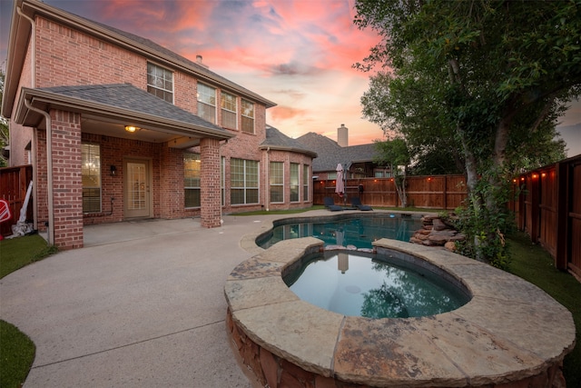 pool at dusk with an in ground hot tub and a patio area