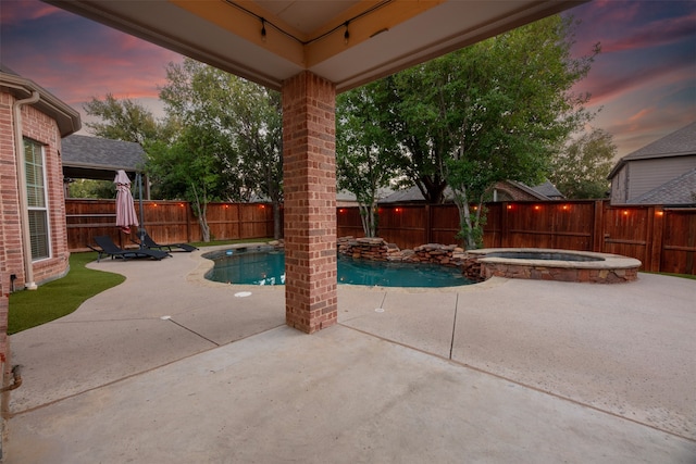 pool at dusk with a patio and an in ground hot tub