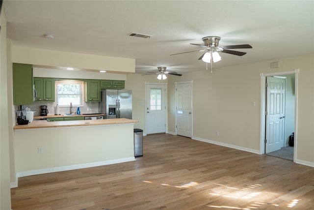 kitchen with kitchen peninsula, green cabinets, light wood-type flooring, and stainless steel fridge