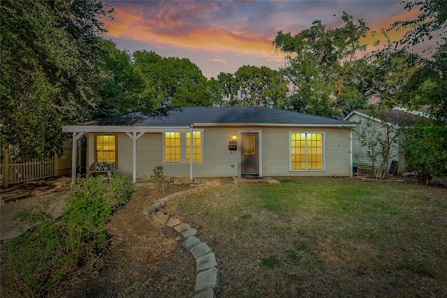 back house at dusk featuring a lawn