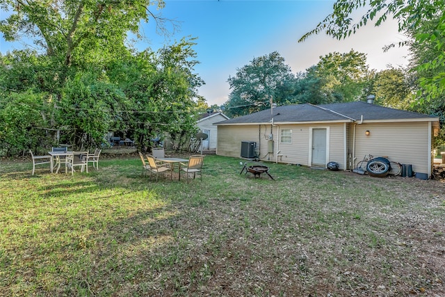 back of property with central air condition unit, a yard, and an outdoor fire pit