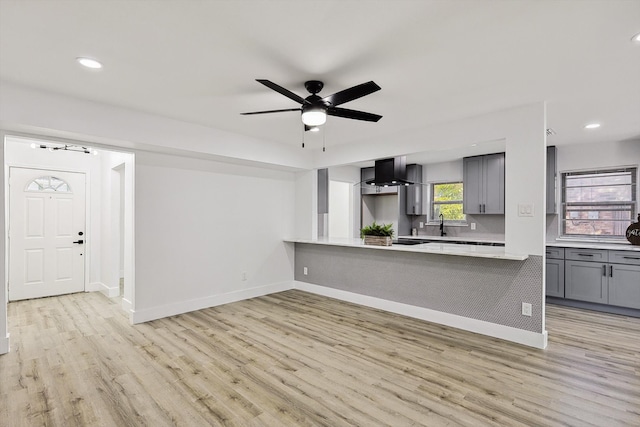 kitchen with ceiling fan, kitchen peninsula, gray cabinetry, light hardwood / wood-style flooring, and wall chimney range hood