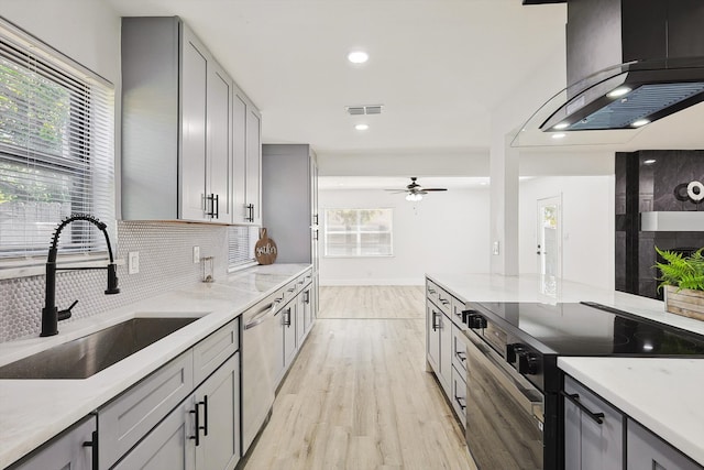 kitchen featuring gray cabinets, light hardwood / wood-style floors, sink, island exhaust hood, and appliances with stainless steel finishes