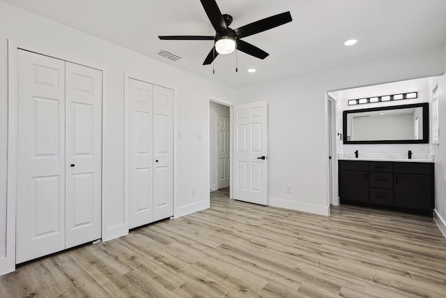 unfurnished bedroom featuring ceiling fan, light hardwood / wood-style flooring, ensuite bathroom, sink, and multiple closets