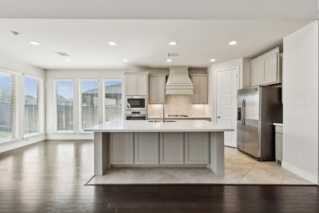 kitchen with premium range hood, sink, a center island with sink, appliances with stainless steel finishes, and light wood-type flooring