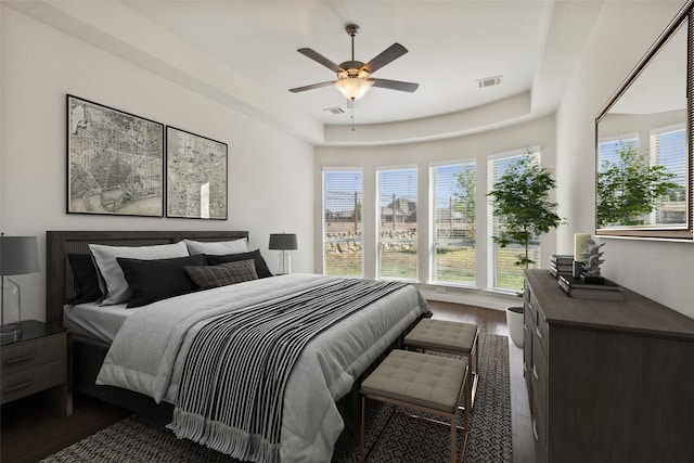 bedroom with a tray ceiling, ceiling fan, and dark wood-type flooring