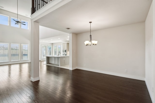 unfurnished room with ceiling fan with notable chandelier, a high ceiling, sink, and dark wood-type flooring