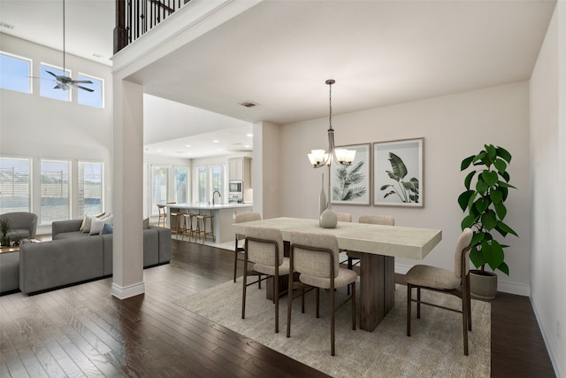 dining area featuring ceiling fan with notable chandelier, a towering ceiling, and dark hardwood / wood-style flooring