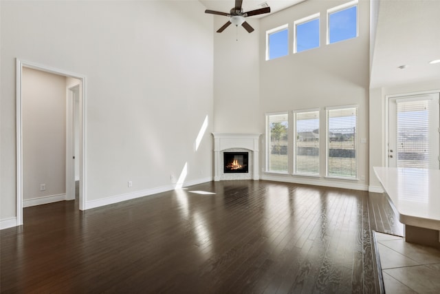 unfurnished living room with a towering ceiling, dark wood-type flooring, and ceiling fan