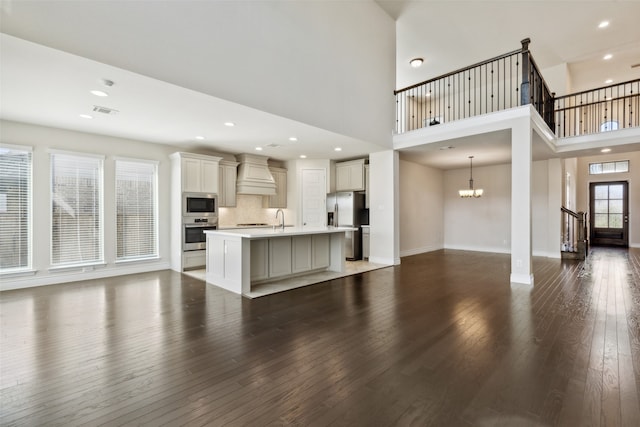 unfurnished living room featuring a towering ceiling, sink, dark wood-type flooring, and a chandelier