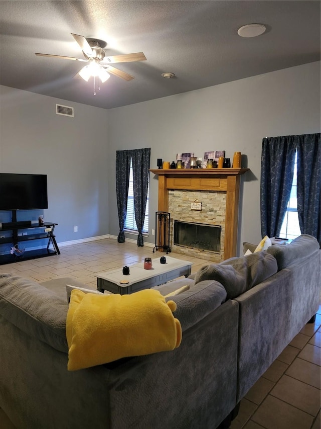 living room with a textured ceiling, ceiling fan, a healthy amount of sunlight, a fireplace, and tile patterned flooring