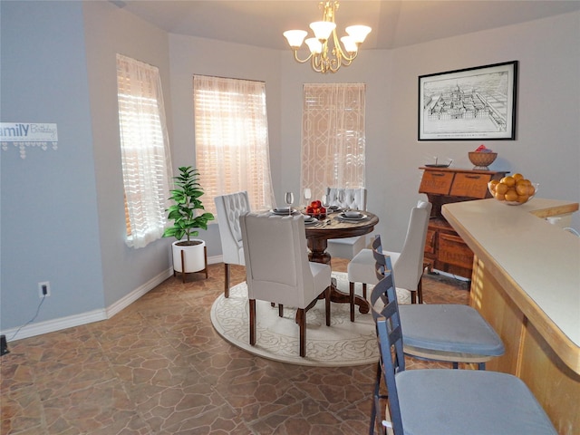 dining space with stone finish floor, plenty of natural light, baseboards, and a chandelier