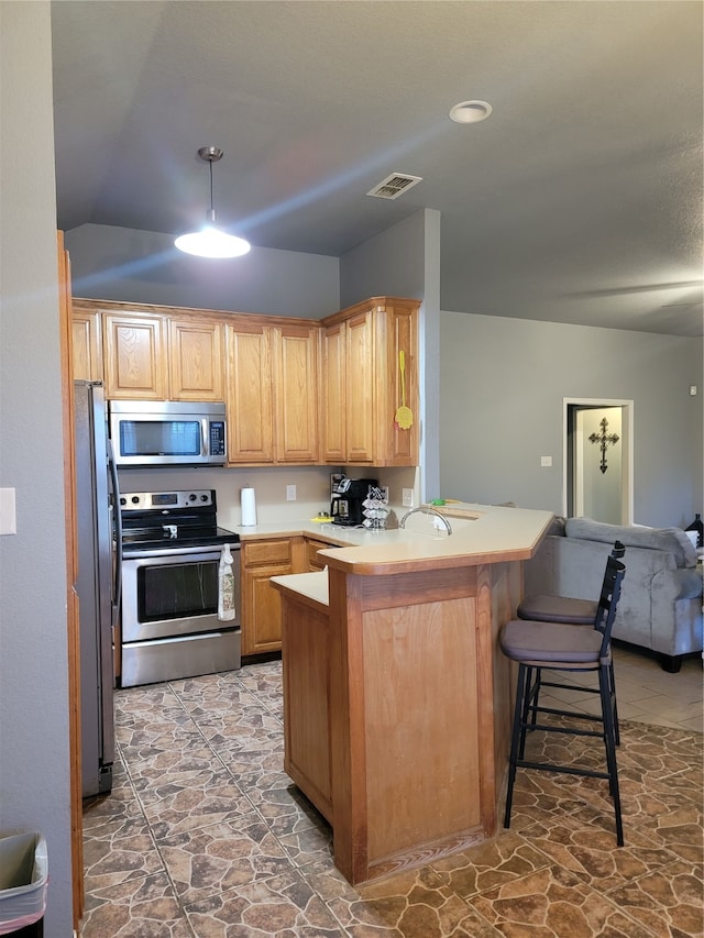 kitchen featuring lofted ceiling, kitchen peninsula, appliances with stainless steel finishes, and a breakfast bar area