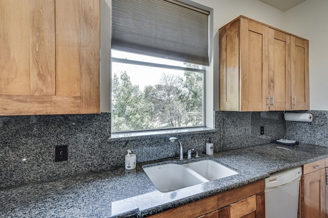 kitchen with white dishwasher, dark stone countertops, tasteful backsplash, and sink