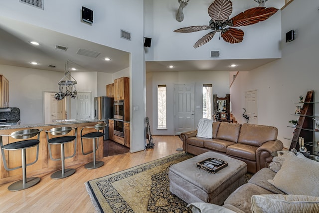 living room featuring ceiling fan with notable chandelier, a towering ceiling, and light hardwood / wood-style flooring