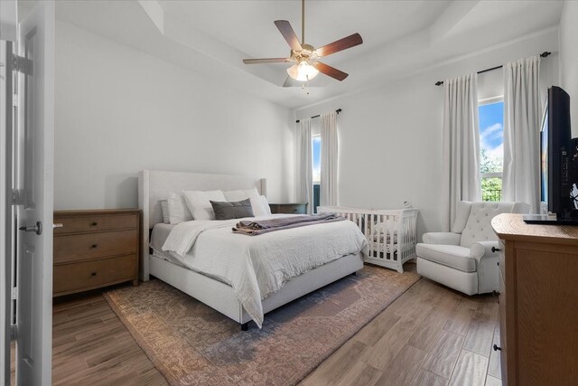 bedroom with ceiling fan, a raised ceiling, and hardwood / wood-style floors