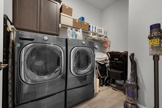 laundry area with washing machine and dryer, light hardwood / wood-style flooring, and cabinets