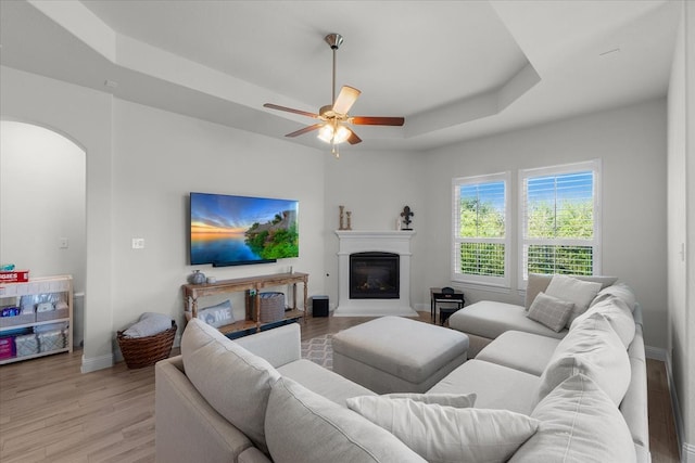 living room with ceiling fan, light wood-type flooring, and a tray ceiling