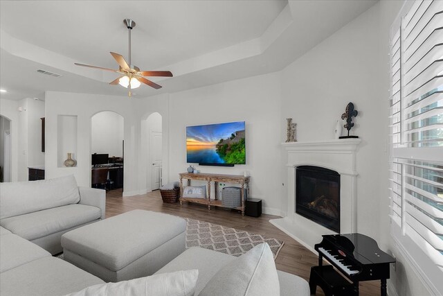 living room featuring wood-type flooring, ceiling fan, and a raised ceiling