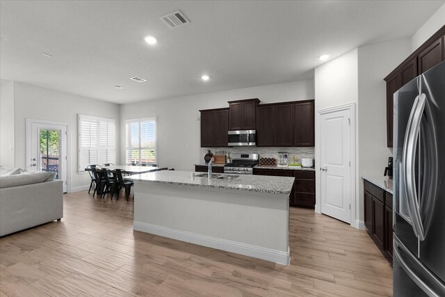 kitchen with light wood-type flooring, sink, an island with sink, stainless steel appliances, and light stone countertops