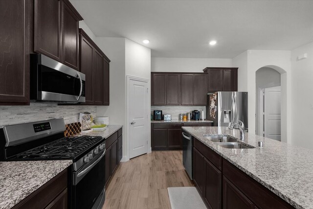 kitchen with dark brown cabinetry, sink, light hardwood / wood-style flooring, backsplash, and appliances with stainless steel finishes