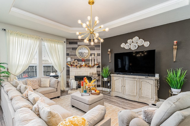 living room with a chandelier, a tray ceiling, a fireplace, light hardwood / wood-style flooring, and ornamental molding