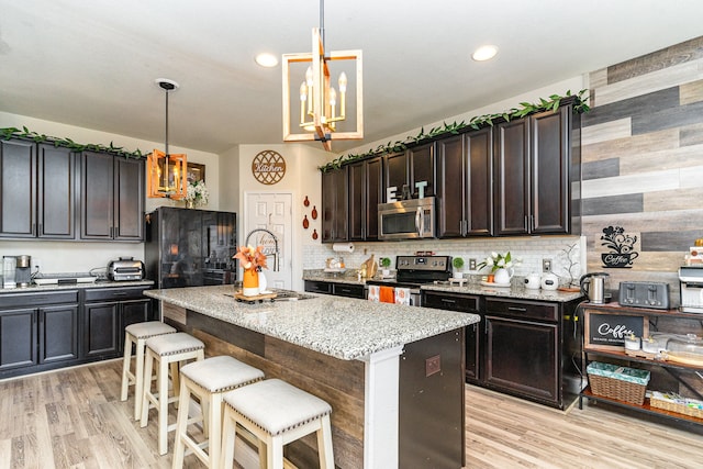 kitchen featuring appliances with stainless steel finishes, a kitchen island, light stone countertops, decorative light fixtures, and dark brown cabinetry