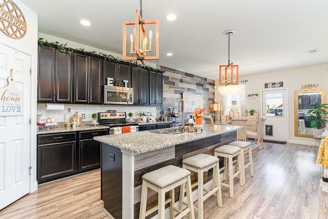 kitchen featuring hanging light fixtures, a kitchen island with sink, stainless steel appliances, a notable chandelier, and light stone countertops