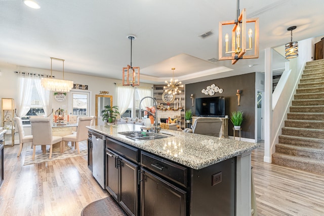 kitchen with decorative light fixtures, a kitchen island with sink, light wood-type flooring, and sink