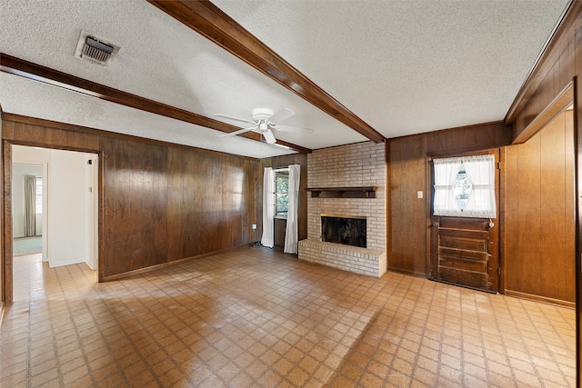 unfurnished living room with a brick fireplace, beamed ceiling, wooden walls, and a textured ceiling