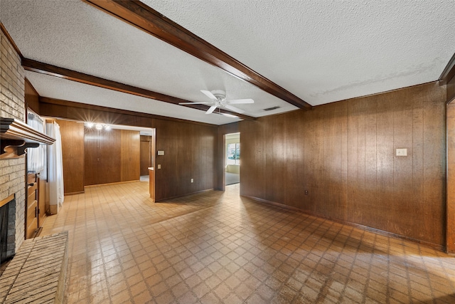 unfurnished living room featuring a textured ceiling, beam ceiling, wood walls, a fireplace, and ceiling fan