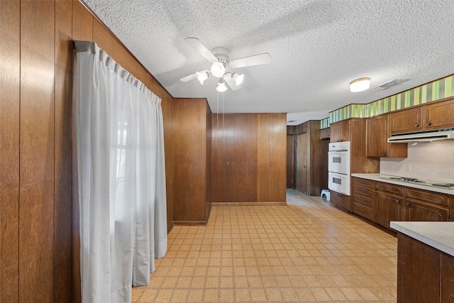 kitchen featuring a textured ceiling, white appliances, wooden walls, and ceiling fan