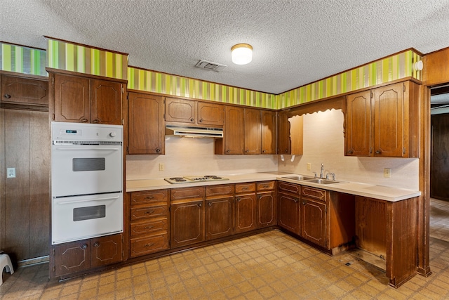 kitchen with a textured ceiling, white appliances, and sink