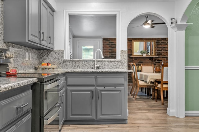 kitchen with light stone counters, gray cabinetry, ornate columns, crown molding, and light hardwood / wood-style flooring