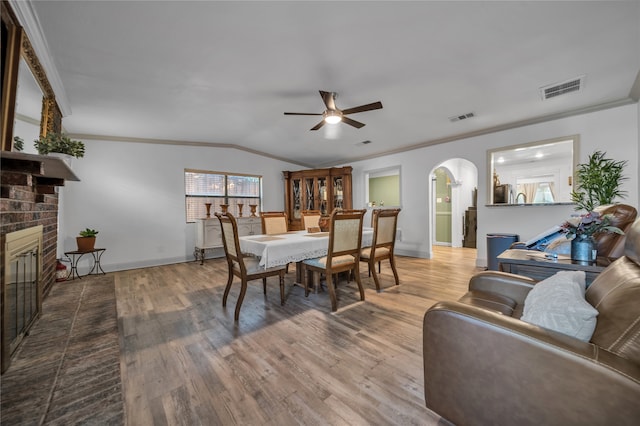 dining room with a brick fireplace, ceiling fan, hardwood / wood-style floors, lofted ceiling, and ornamental molding