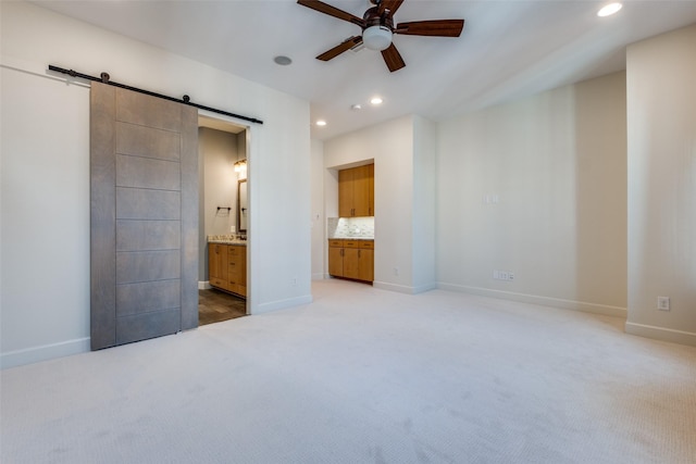 unfurnished bedroom with light carpet, ceiling fan, ensuite bathroom, and a barn door