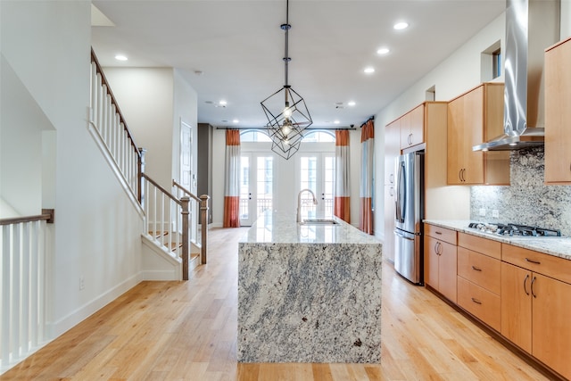 kitchen with stainless steel fridge, decorative light fixtures, a kitchen island with sink, gas stovetop, and light stone countertops