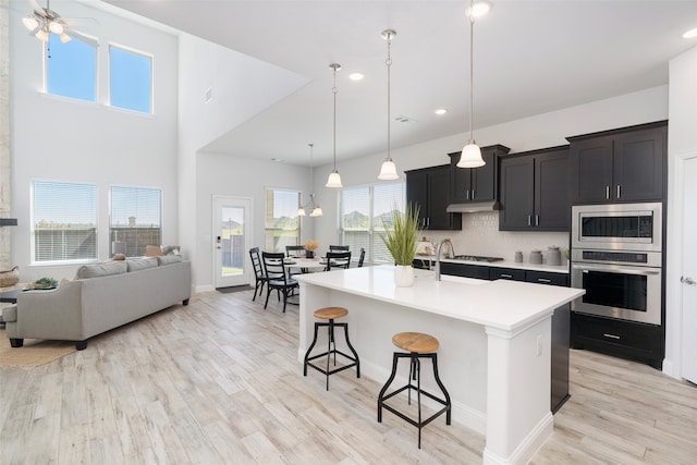 kitchen featuring an island with sink, decorative light fixtures, appliances with stainless steel finishes, a breakfast bar area, and light wood-type flooring