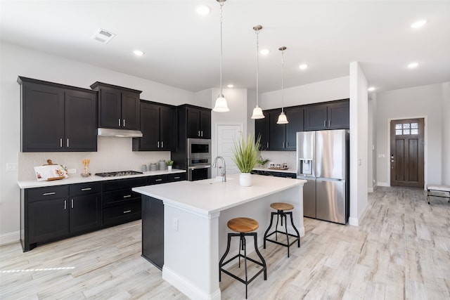 kitchen featuring a kitchen island with sink, a breakfast bar area, hanging light fixtures, light hardwood / wood-style flooring, and stainless steel appliances