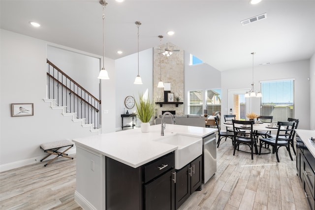 kitchen with light hardwood / wood-style floors, a kitchen island with sink, sink, decorative light fixtures, and stainless steel dishwasher