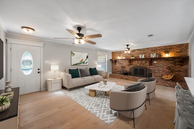 living room featuring crown molding, a fireplace, ceiling fan, and light wood-type flooring